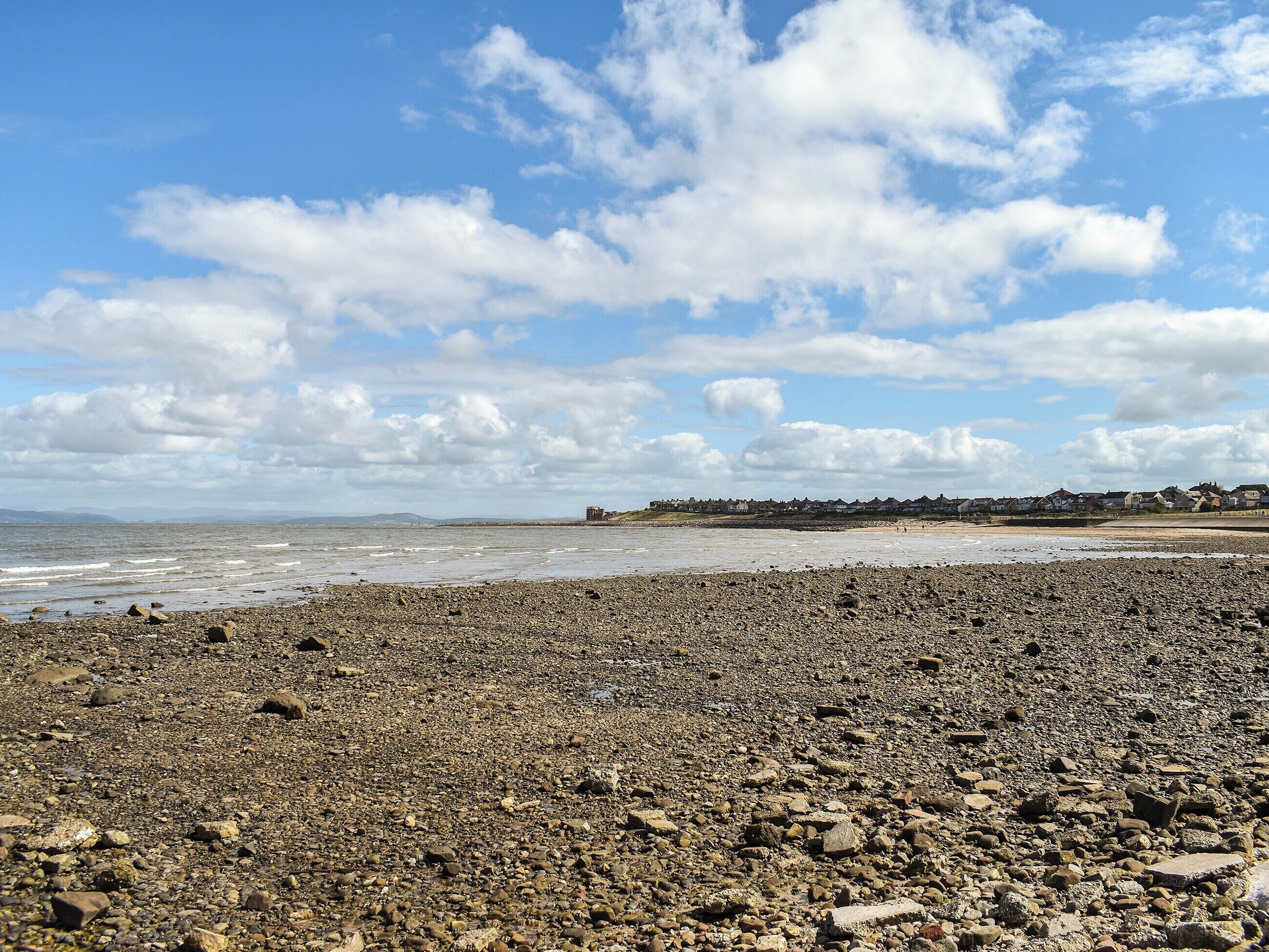 Une plage de galets avec une rangée de maisons en arrière-plan.