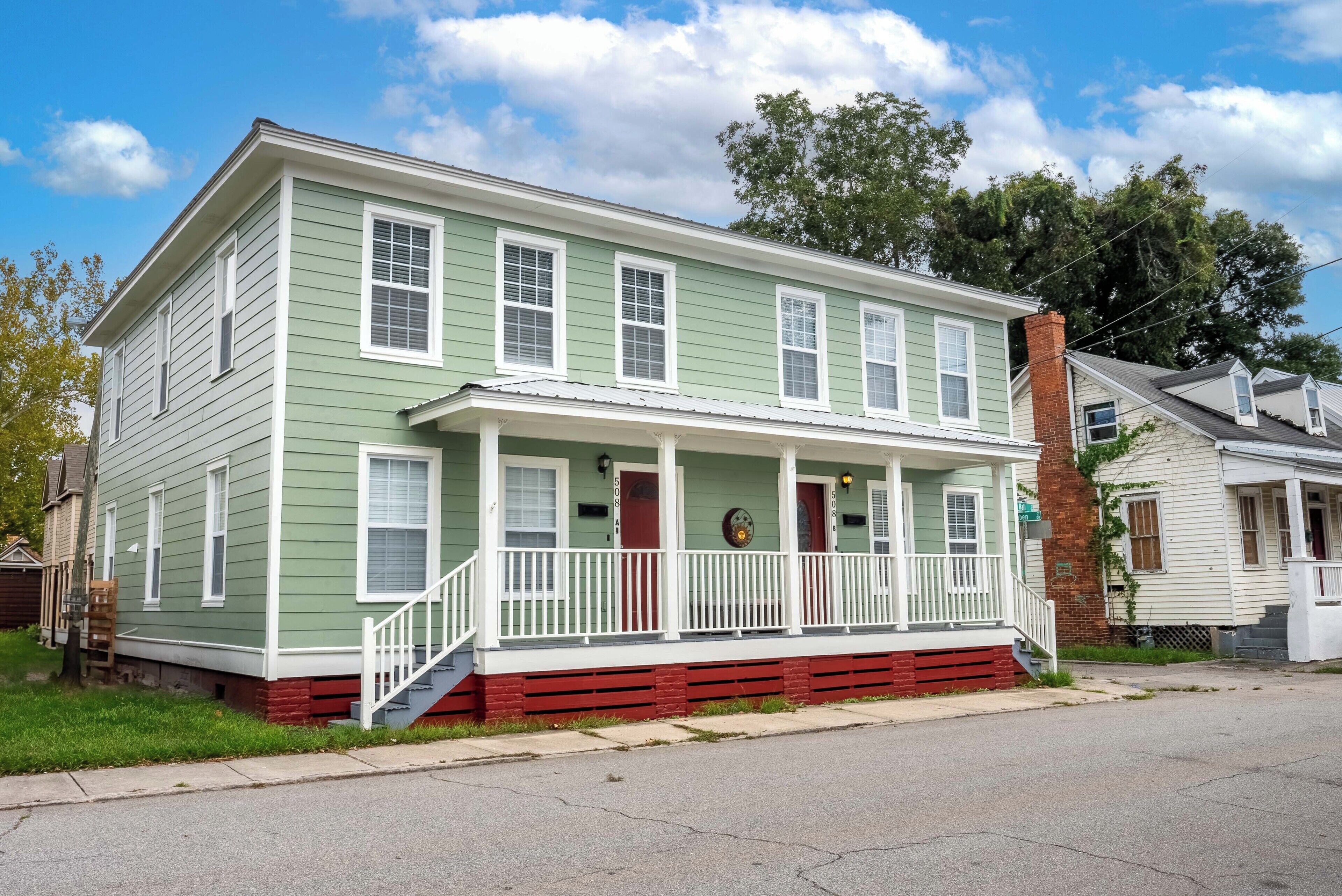 A two-story house with a front porch, a brick chimney, and a small front yard.