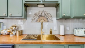 Een keuken met groene kastjes, een gouden kraan en een decoratieve ventilator.