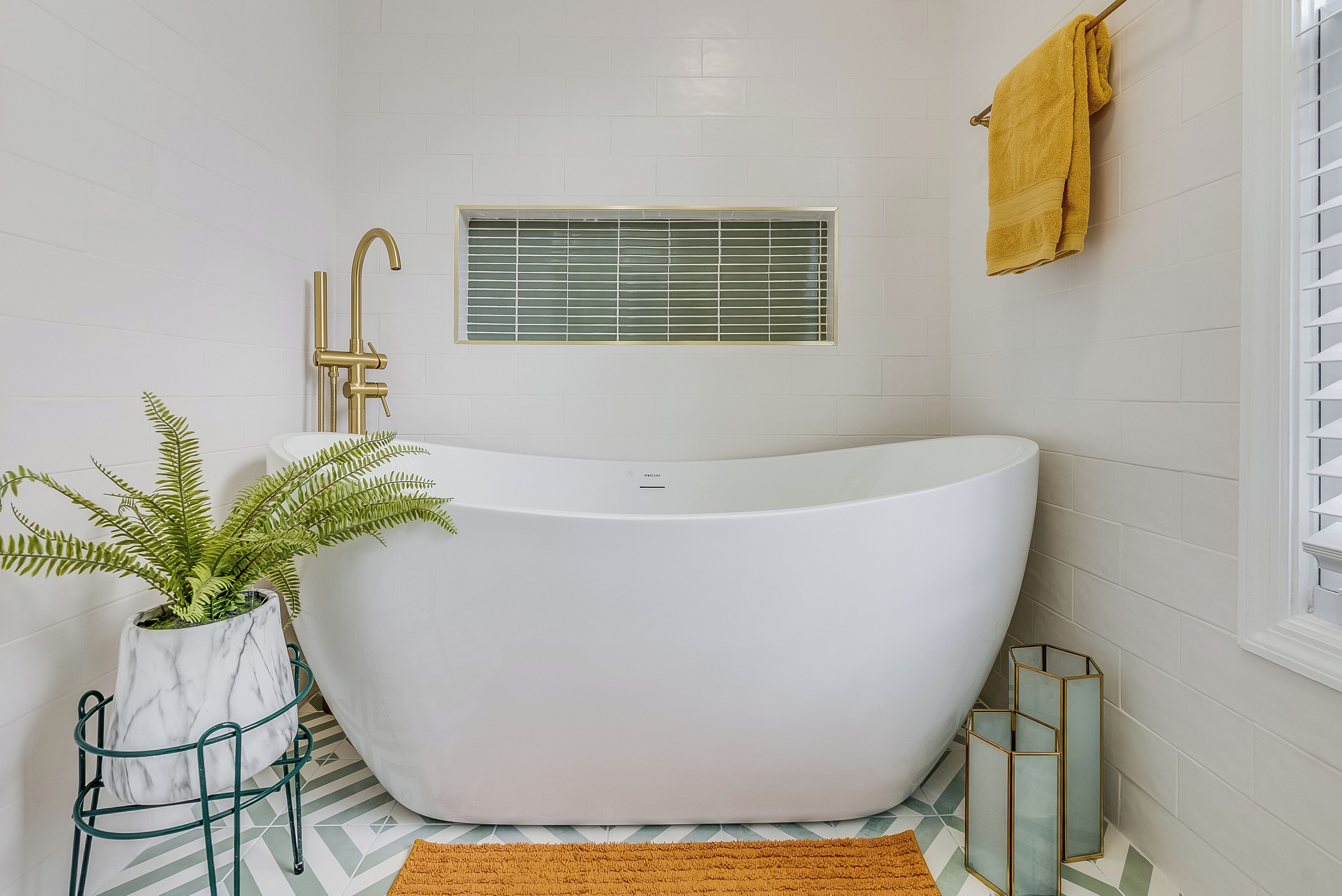 Ein modernes Badezimmer mit einer freistehenden Badewanne, einem Fenster mit Jalousien, einem Blumentopf und einem Handtuchhalter.
