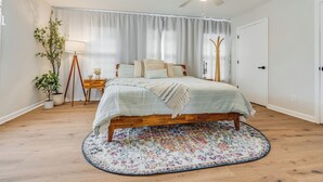 Een slaapkamer met een bed, een plafondventilator, een raam met gordijnen, een nachtkastje met lamp en een kamerplant.
