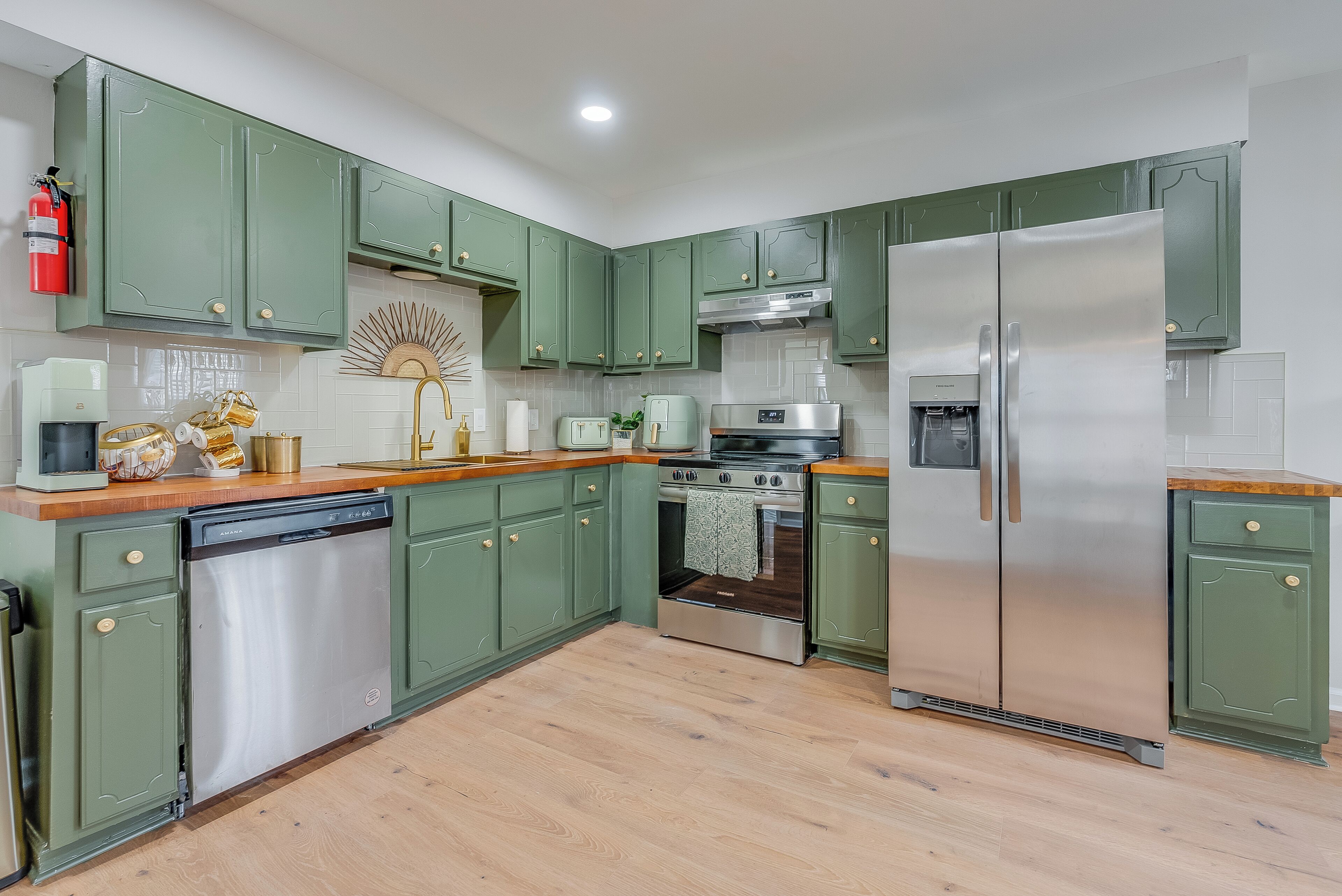 A kitchen with green cabinets, stainless steel appliances, and a wooden countertop.