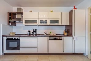 Eine moderne Küche mit weißen Schränken, einem Einbauofen, einer Kaffeemaschine und einem Geschirrspüler.