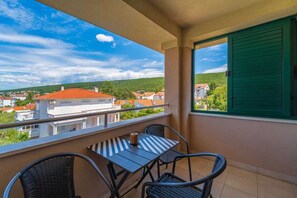Ein Balkon mit Tisch und Stühlen, Blick auf Gebäude und ein Fenster mit grünen Rollläden.
