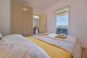Une chambre avec un lit, une armoire, un balcon avec des chaises et une vue sur le ciel.
