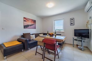 Un salon moderne comprenant un canapé, une table à manger, des chaises, un téléviseur et des œuvres d’art accrochées aux murs.