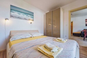 Ein Schlafzimmer mit einem Bett, einem Meeresbild, einer Schiebetür und einem Sessel in der Ecke.