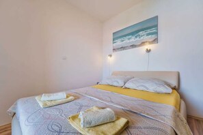 Une chambre à coucher avec un lit, des serviettes, un tableau représentant la mer et une veilleuse.