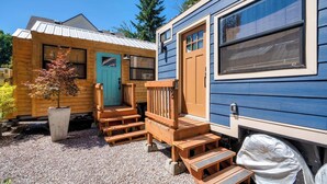 A small wooden cabin with a blue exterior, a wooden porch with steps, and a potted tree. - Tiny Farmhouse - Walk to Local Shops & Restaurants (Portland)