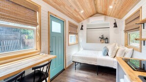 A compact room with a wooden ceiling, a bed, a table with chairs, and a window with blinds. - Tiny Farmhouse - Walk to Local Shops & Restaurants (Portland)