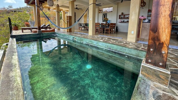 Een zwembad met helder water, een houten terras, ligbedden en een eethoek met een tafel en stoelen.