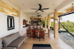 A dining area with a table and chairs, a ceiling fan, and a kitchen in the background. - Luxury Villa with Infinity Pool and Ocean Views (Mazunte)