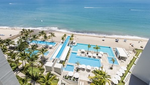 Een resort met meerdere zwembaden, een strand en palmbomen.
