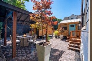 A patio area with a fire pit, outdoor seating, and a wooden structure. - The Sunstone • Modern Tiny House • Prime Location (Portland)