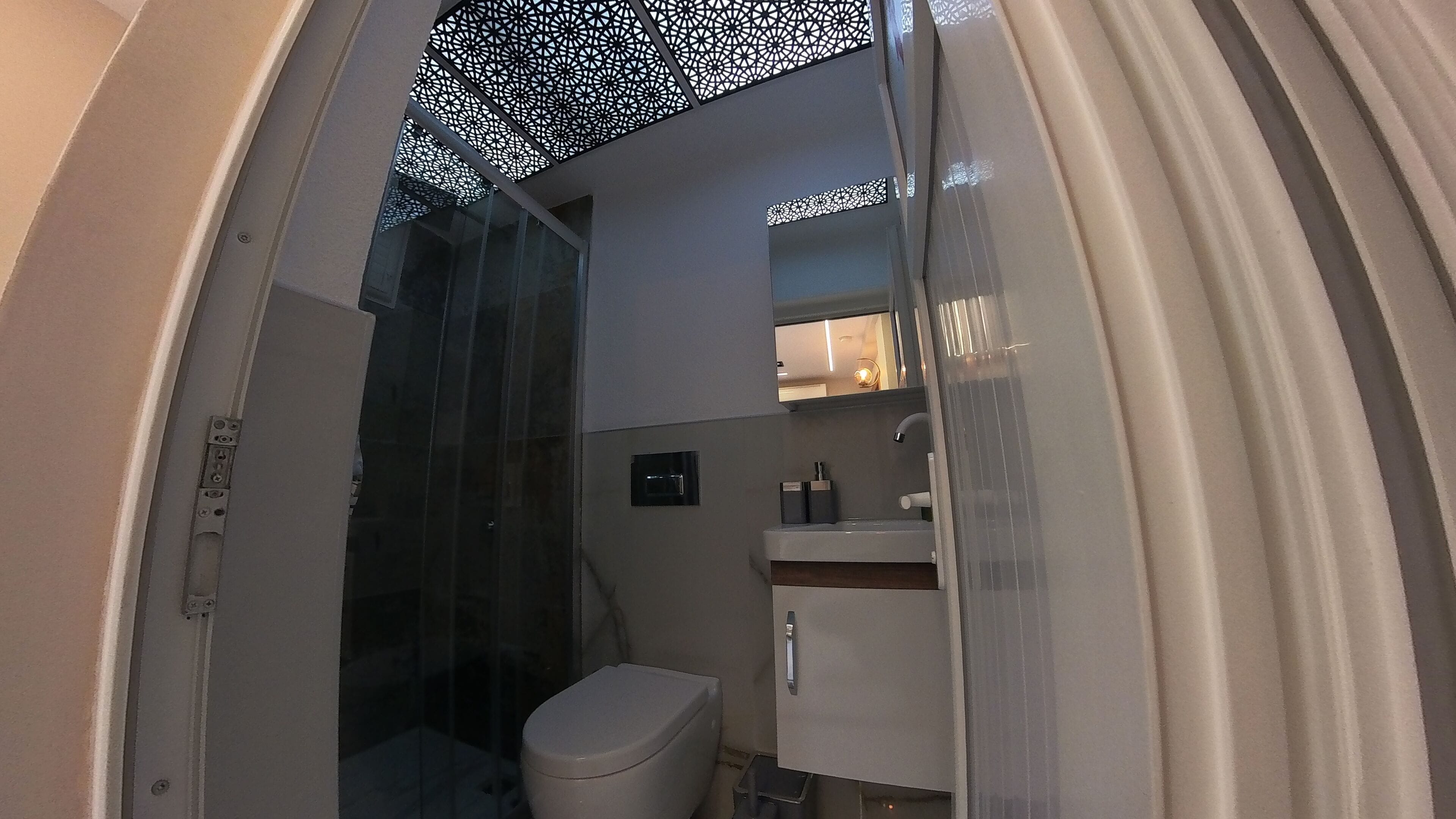 A modern bathroom with a glass shower enclosure, a toilet, a sink with a mirror, and a cabinet.
