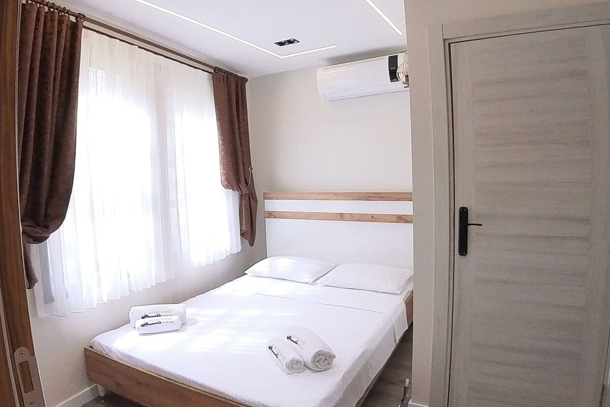 Un dormitorio con una cama de madera, ropa de cama blanca, una lámpara en el techo y una puerta.