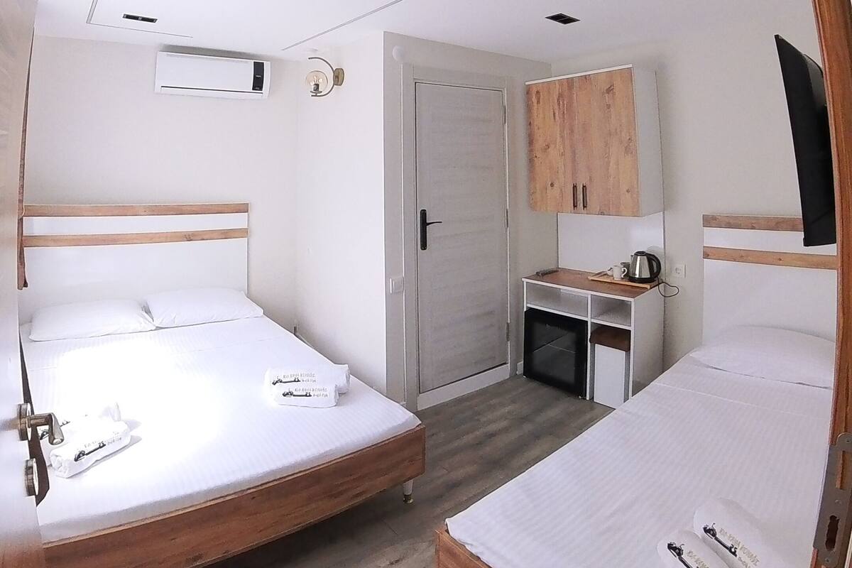 Una habitación de hotel compacta con dos camas, una kitchenette, un armario y un televisor.