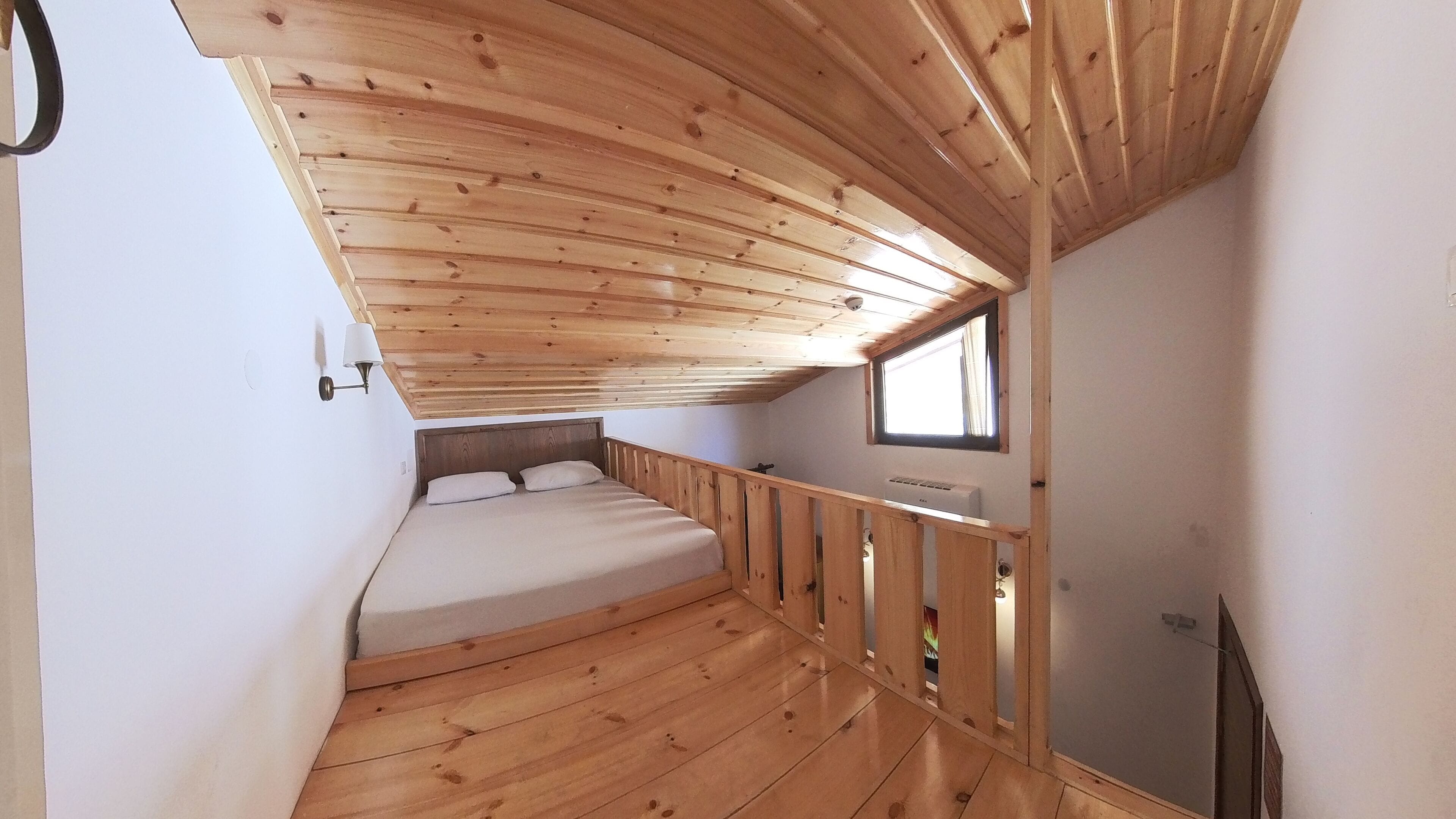 A compact room with a wooden ceiling, a single bed, a small window, and a wall-mounted heater.