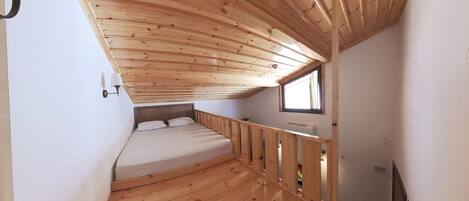 A compact room with a wooden ceiling, a single bed, a small window, and a wall-mounted heater.