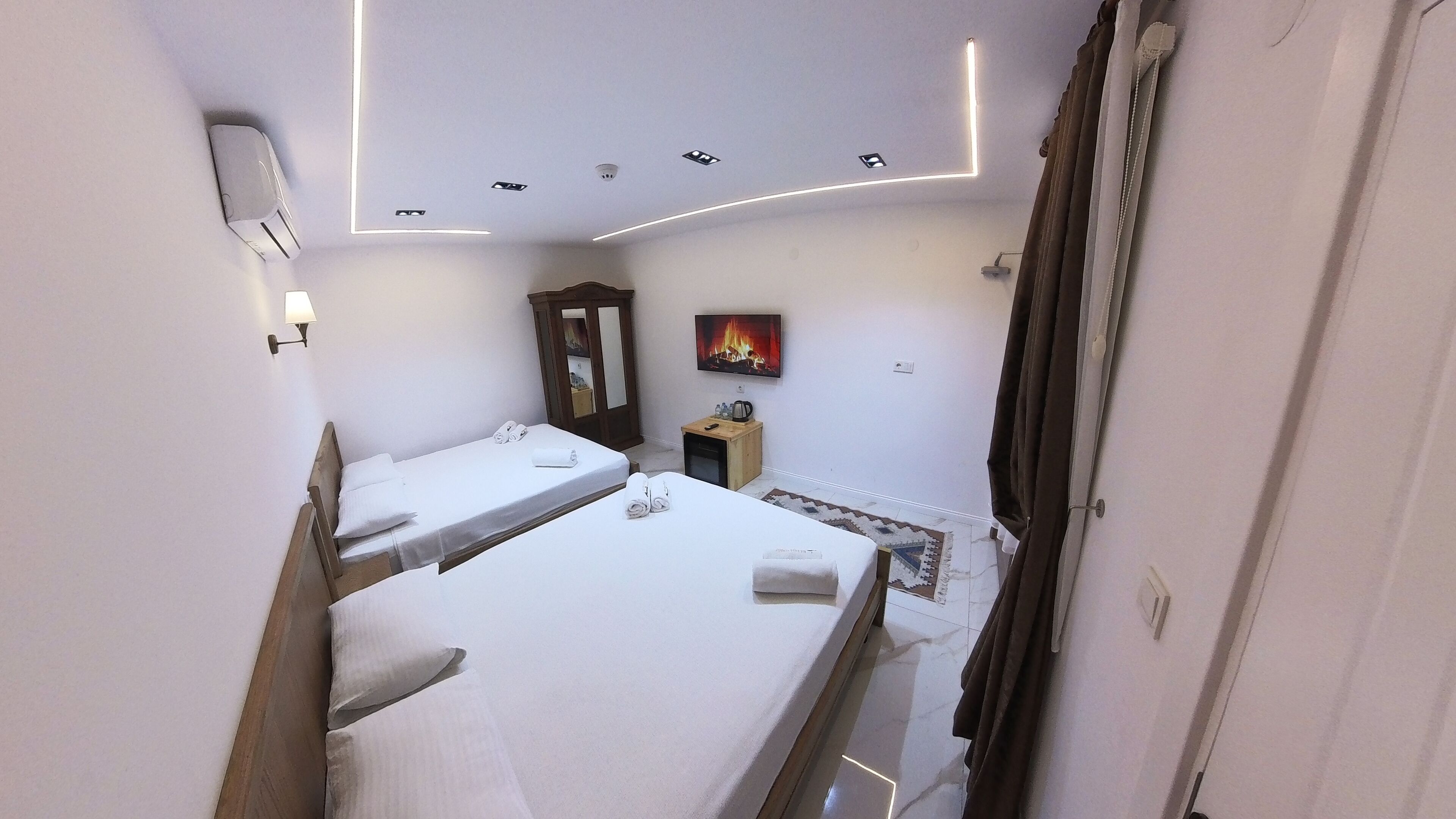 A hotel room with two beds, a small wooden cabinet, a wall-mounted TV, and a ceiling light fixture.