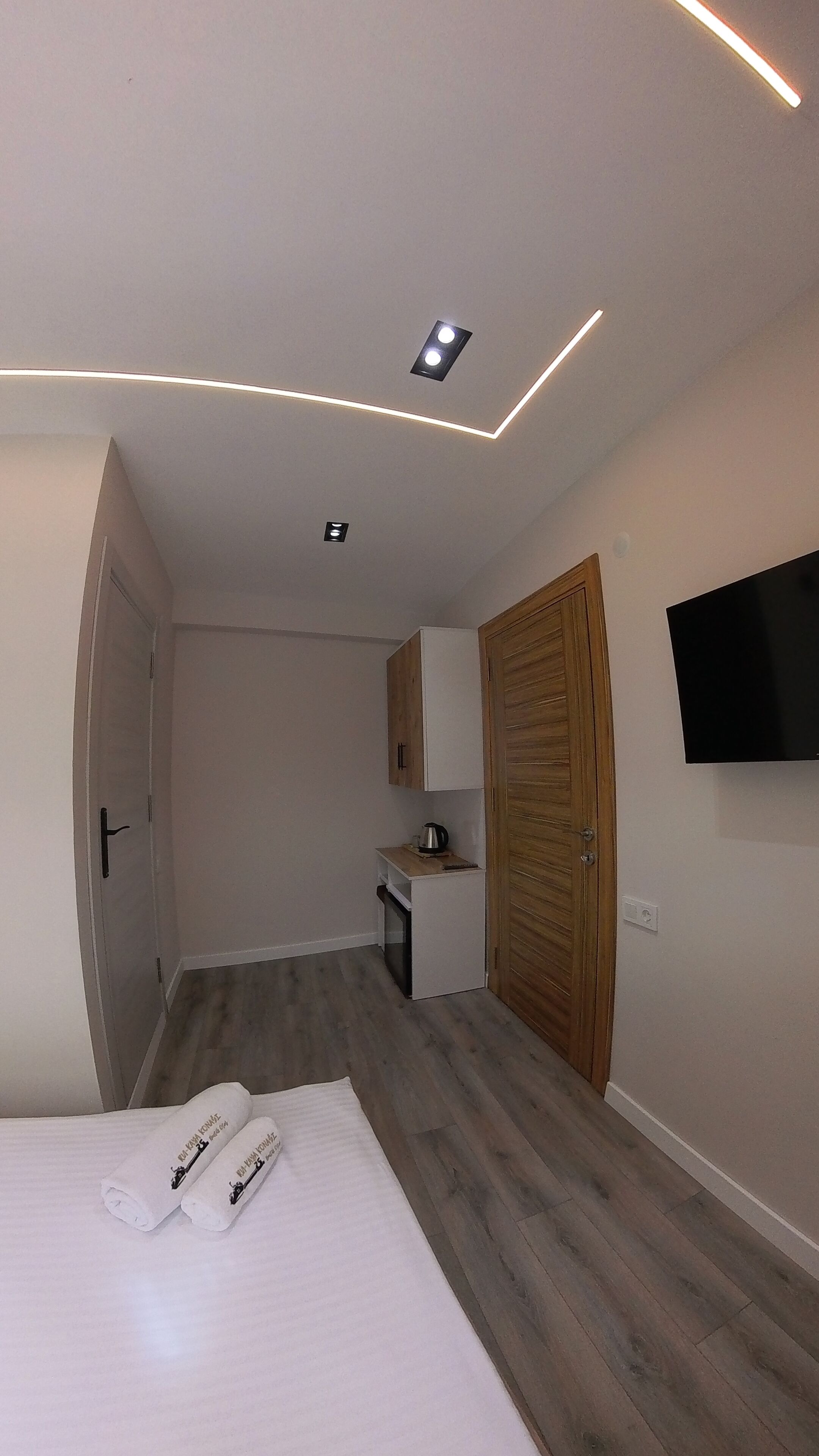 Una habitación de hotel moderna con una cama, un armario de madera, una pequeña kitchenette y un televisor de pantalla plana montado en la pared.