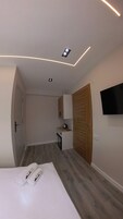 Una habitación de hotel moderna con una cama, un armario de madera, una pequeña kitchenette y un televisor de pantalla plana montado en la pared.
