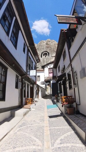 A narrow cobblestone street flanked by white buildings with black window frames and wooden benches. - Rukaya Konağı (Amasya)