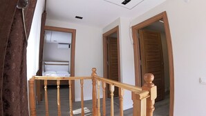 Een houten trap met een leuning, die leidt naar een kamer met een bed en een airconditioner aan de muur.