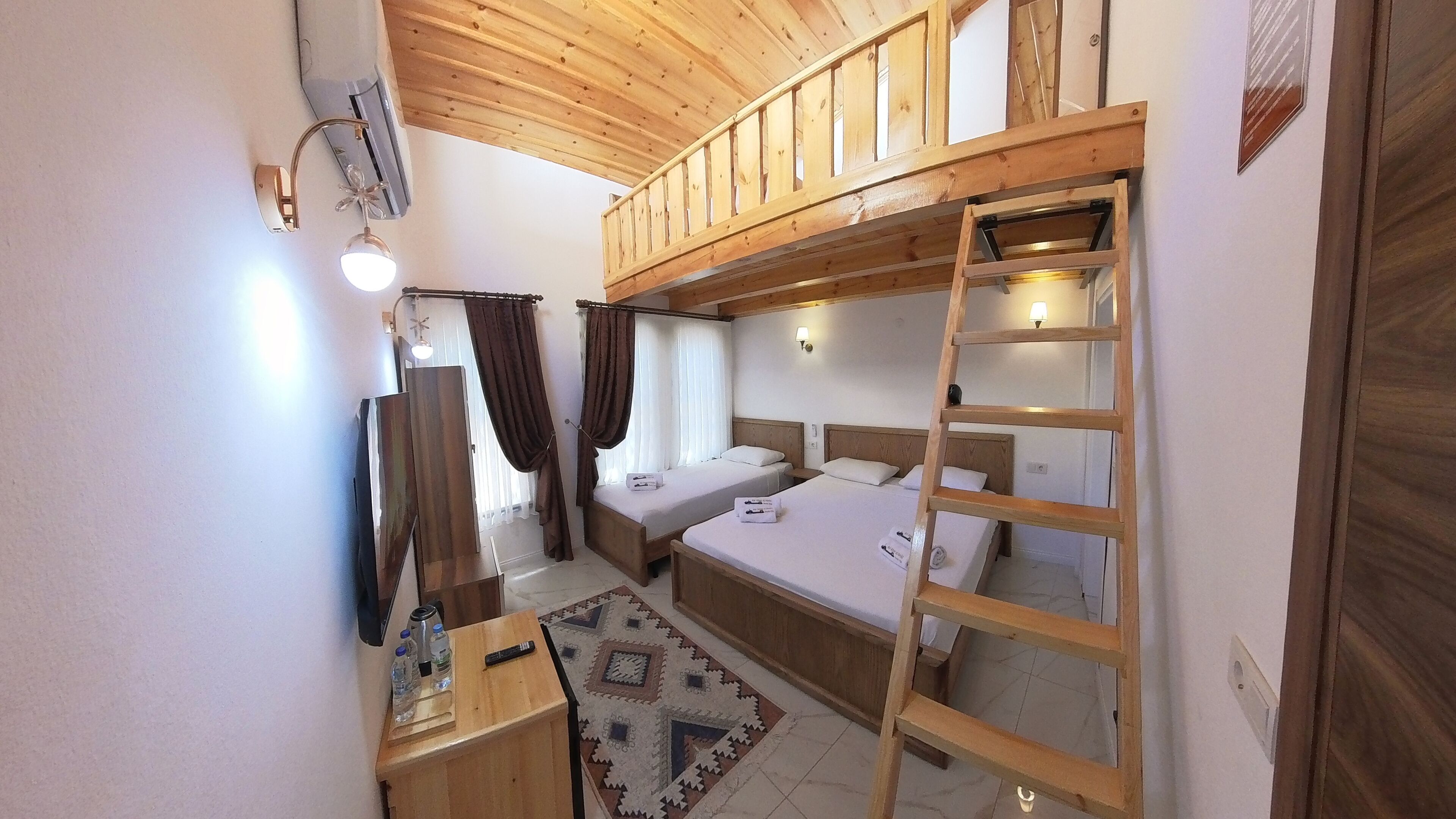 A compact room with two beds, a wooden ladder, a desk with a mirror, and a small rug.