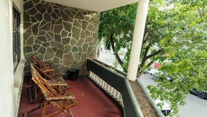 Un espacio de estar al aire libre con techo, sillas de madera, un muro de piedra y vistas a la calle.