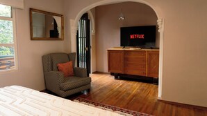 Una habitación con una cama, una silla, un televisor que muestra 'NETFLIX' y un armario de madera.