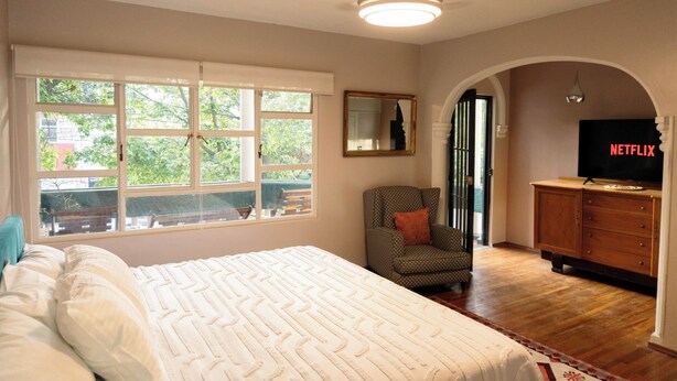 Un dormitorio con cama, una silla, un televisor y una ventana con vistas a zonas verdes.