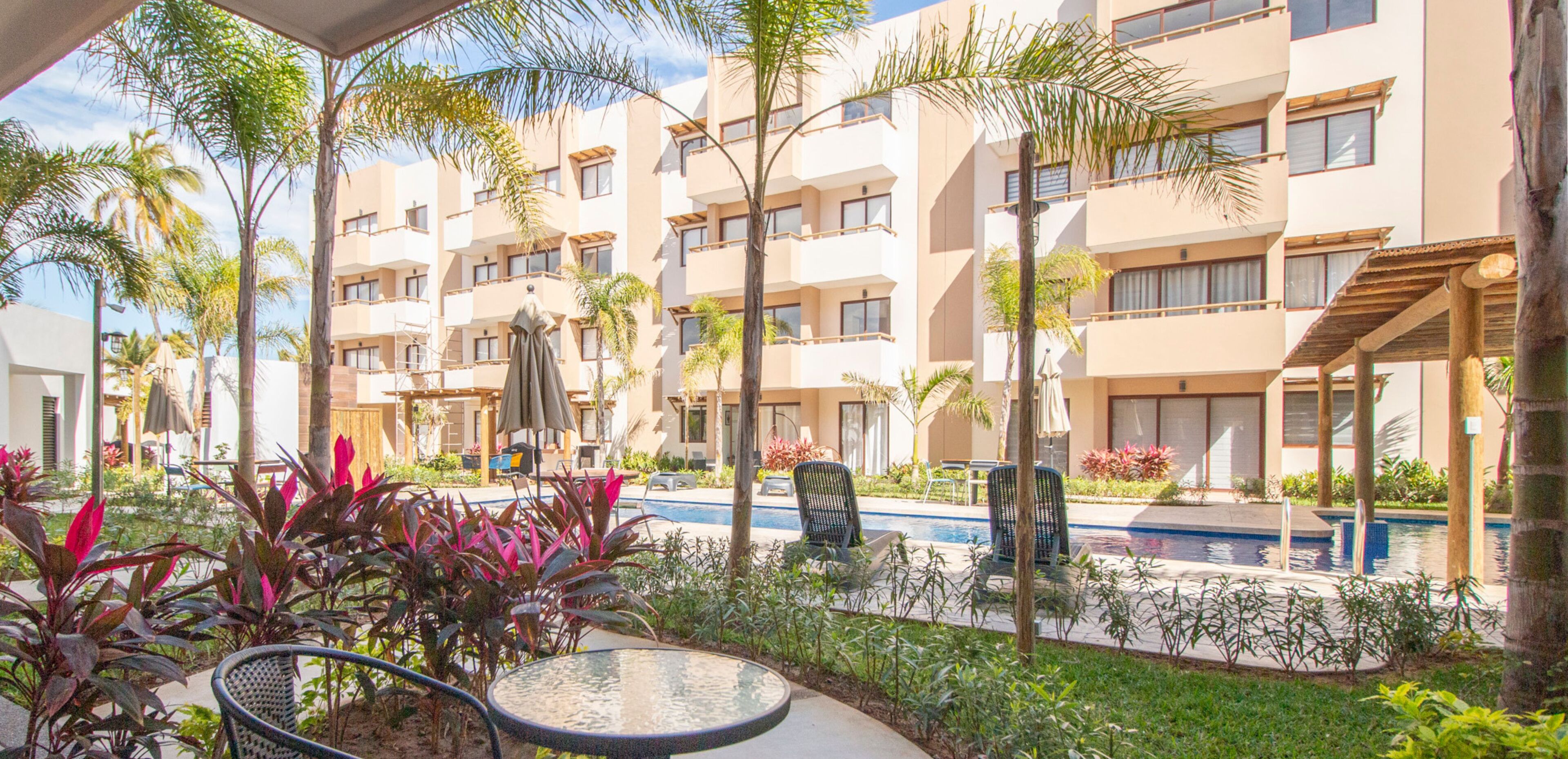 Un patio de hotel con piscina, mobiliario exterior y palmeras.