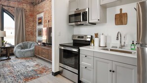 A modern kitchen with white cabinets, stainless steel appliances, a brick wall, and a cozy seating area. - Cozy 1-bedroom apartment in fabulous Wabash with WiFi, AC (Wabash)