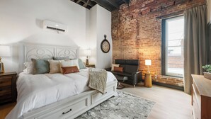A bedroom with a white bed, a brick wall, a fireplace, and a window with curtains. - Cozy 1-bedroom apartment in fabulous Wabash with WiFi, AC (Wabash)