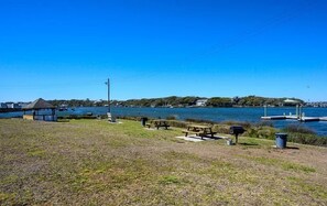 Un espace de pique-nique au bord du lac, équipé de bancs et d’un petit abri, entouré de berges verdoyantes et surplombé d’un ciel bleu clair.