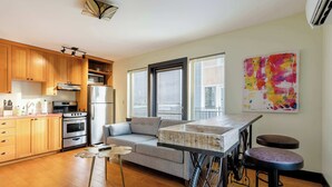 A modern kitchen with wooden cabinets, stainless steel appliances, a gray sofa, and a bar stool.