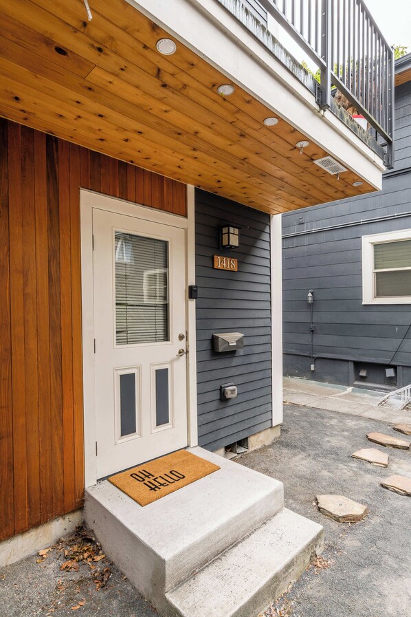 A wooden porch with a white door, a mailbox, and a stone pathway leading to the entrance.