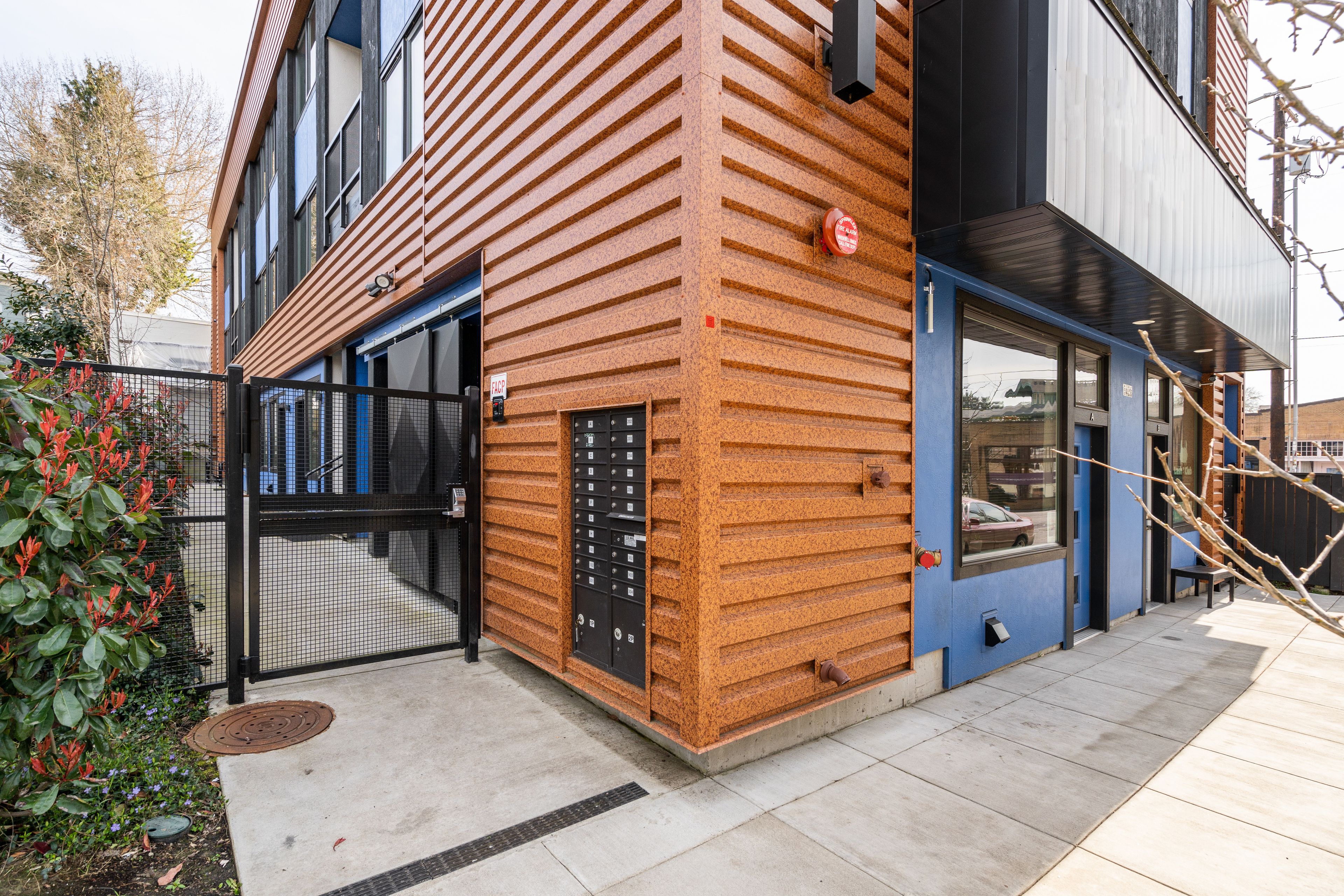 A modern building with a distinctive wooden facade, a fire alarm, and a gated entrance.