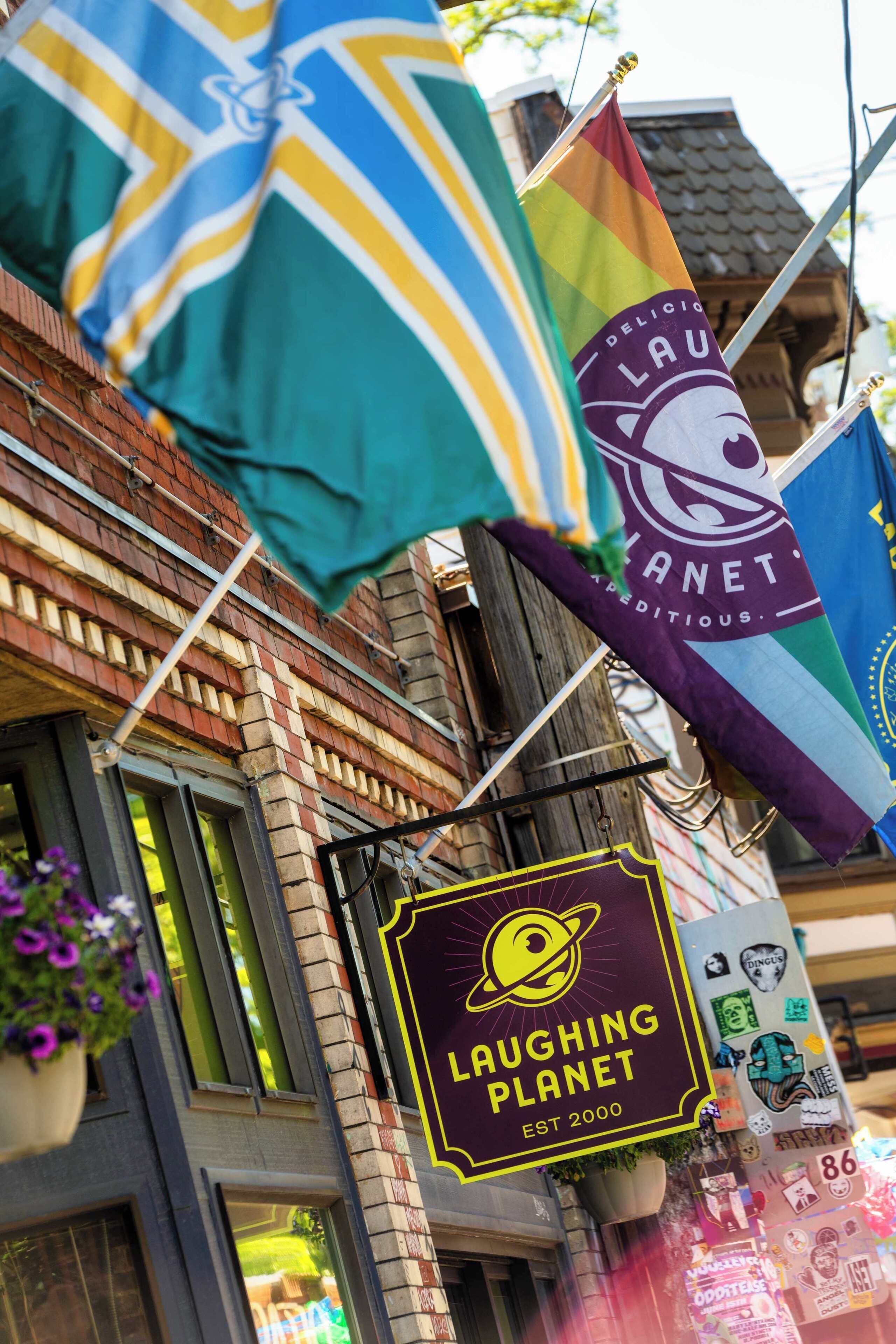 Un bâtiment orné de plusieurs drapeaux, dont l’un porte l’inscription « LAU » et l’autre « LAUGHING PLANET EST 2000 ».