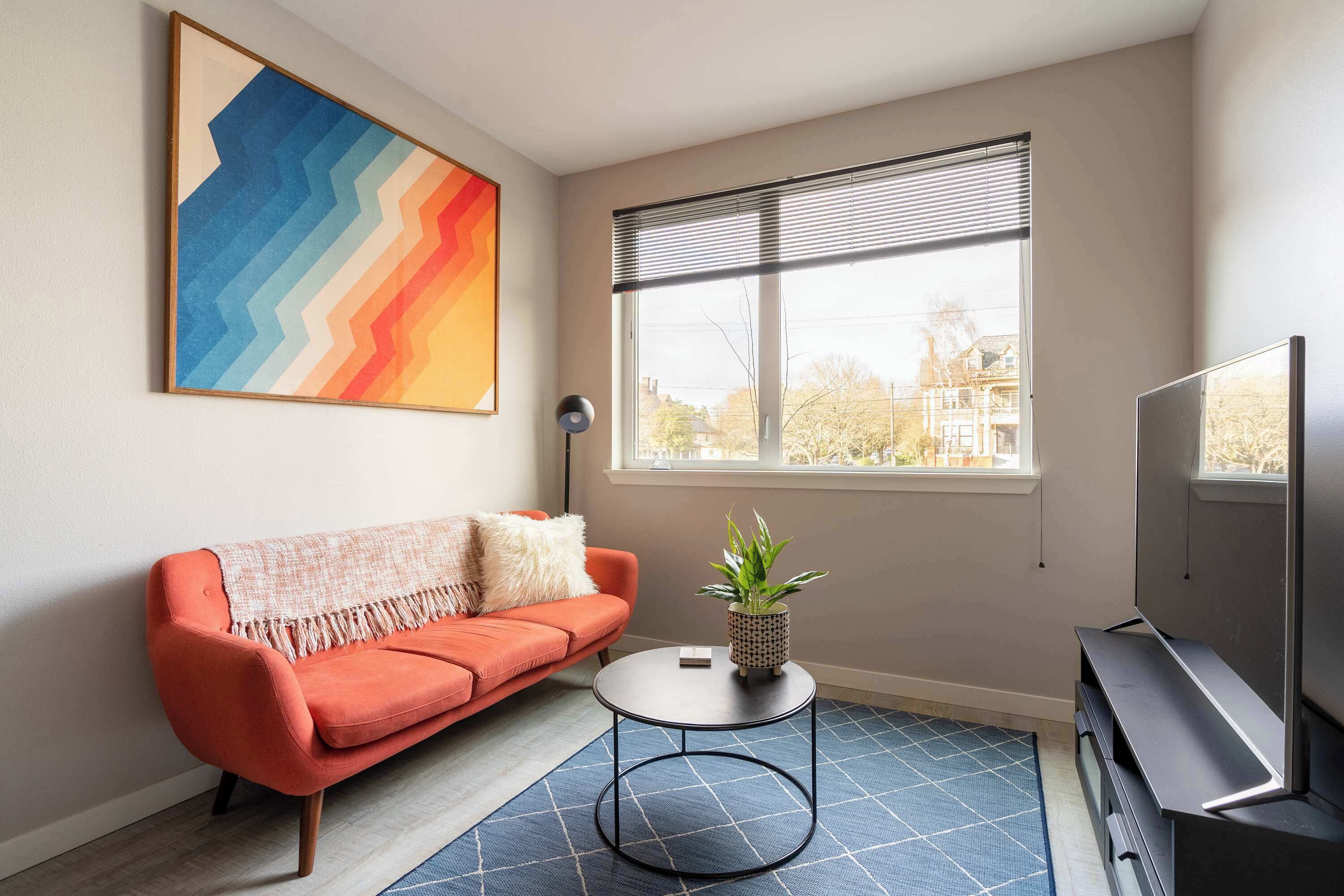 A modern living room with a sofa, a round coffee table, a TV, and a window with blinds.