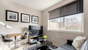 Una sala de estar moderna con un sofá de cuero negro, una mesa de centro de vidrio, un televisor y cuadros en la pared.