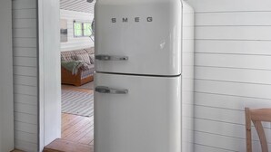 Valkoinen Smeg-jääkaappi huoneessa, jossa on valkoiset paneeliseinät ja puulattia.