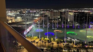 A nighttime view of a cityscape with illuminated buildings and a large, open plaza with circular patterns and tall poles. - MGM Signature Balcony One Bedroom Two Beds Suite (Las Vegas)