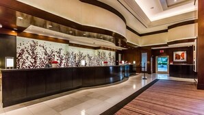 Eine moderne Hotelhalle mit einer geschwungenen Rezeption, einer großen abstrakten Wandkunst und einem geräumigen Bereich mit einem gemusterten Teppich.