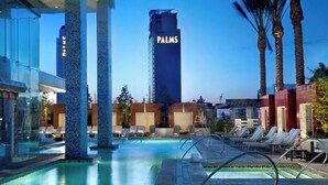 A hotel pool area with lounge chairs, a large water feature, and a tall building labeled "PALMS" in the background.