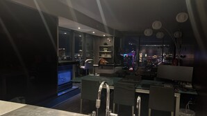 A modern kitchen with a large island, stainless steel appliances, and a view of the cityscape at night.
