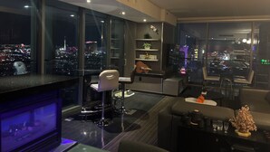A modern living room with a city view, a bar area, and a dining space.