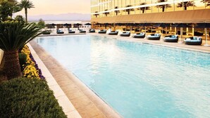 Une grande piscine intérieure dotée de chaises longues et de parasols, entourée d’un aménagement paysager soigné et d’un bâtiment moderne aux grandes fenêtres.