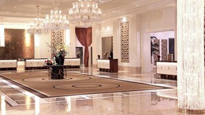 Un hall d’entrée spacieux, agrémenté d’un grand lustre, d’un comptoir de réception et d’un vase décoratif rempli de fleurs.